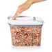 A hand reaching into a clear rectangular OXO plastic food storage container with granola inside.