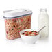 An OXO clear rectangular food storage container filled with cereal next to a bowl of cereal.