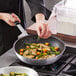 A person cooking meat and vegetables in a Vollrath Arkadia non-stick fry pan.