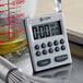 A silver CDN digital kitchen timer on a metal surface next to a measuring cup.