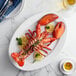 A cooked Boston Lobster Company lobster on a plate with lemon slices and sauce.
