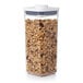 An OXO Good Grips square plastic food storage container with granola and nuts inside and a white lid.