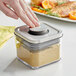 A person using an OXO Good Grips square plastic food storage container with a stainless steel lid to store food.