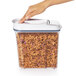 A hand holding a clear rectangular OXO plastic food storage container filled with cereal.
