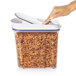 A hand pressing a white OXO Good Grips plastic lid on a container of cereal.
