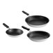 A group of three Vollrath stainless steel frying pans with black and white interiors and black silicone handles.