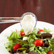 A clear plastic ladle spooning white sauce over a salad.