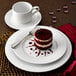 A white porcelain plate with a slice of red velvet cake and a cup of coffee on a saucer.