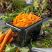 A Carlisle black plastic food pan filled with shredded carrots on a table in a salad bar.