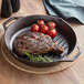 A steak and tomatoes cooking in a Lodge cast iron grill pan.