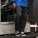 A person wearing Uncommon Chef black cargo chef pants standing on a metal platform.