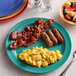 A plate of scrambled eggs, bacon, sausage, and fruit on a Brazil melamine plate.
