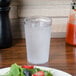 A Carlisle clear plastic tumbler filled with water next to a plate of salad.