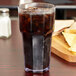 A Carlisle clear plastic tumbler filled with soda on a table with chips and salsa.