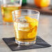 An Acopa Select old fashioned glass with ice and an orange slice.