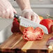 A person cutting a tomato with a Wusthof Classic Ikon Santoku Knife.