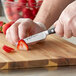 A hand uses a Wusthof Classic Ikon paring knife to cut a strawberry on a cutting board.