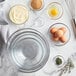 A clear glass Anchor Hocking mixing bowl filled with egg yolks on a marble surface.