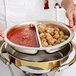 A chef uses a Vollrath stainless steel 2-compartment round food pan to serve meatballs and sauce at an outdoor catering event.