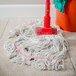 A Carlisle natural cotton looped end wet mop with a red headband in use on a floor with a bucket.