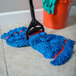 A Carlisle blue microfiber wet mop with a handle on the floor next to a mop bucket.
