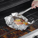 A person using tongs to grill salmon in foil.