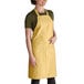 A woman wearing a gold Intedge bib apron with pockets.