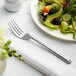 An Acopa Iris stainless steel salad fork on a plate of salad.