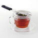 An OXO stainless steel strainer filled with tea sits on a glass cup.