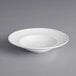An Acopa Liana bright white porcelain soup bowl with embossed lines on a gray surface.