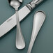 A close-up of a Sant'Andrea Bellini stainless steel oval bowl soup / dessert spoon and a knife on a table.