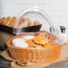 A clear round polyweave cover on a basket of pastries and bread on a counter.