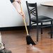 A person using a Carlisle 3-stitch lobby corn broom to sweep the floor.