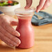 A hand holding a Choice polycarbonate carafe with a flat lid of pink liquid.