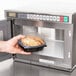 A hand placing a container of food in a Panasonic commercial microwave.