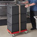 A man pushing a stack of black Cambro Cam GoBoxes on a red Cambro Compact Camdolly.