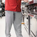 A man wearing Uncommon Chef Houndstooth chef pants and a red jacket standing in a professional kitchen.