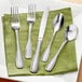A close-up of Acopa Saxton stainless steel flatware on a green napkin with a fork and spoon.