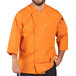 A man wearing a Uncommon Chef 3/4 length sleeve chef coat in orange with carrots on the counter.