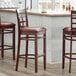 A Lancaster Table & Seating mahogany wood bar stool with a burgundy vinyl seat.