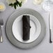 A 10 Strawberry Street silver charger plate with a black napkin and silverware on a table.