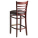 A Lancaster Table & Seating mahogany wood bar stool with a dark brown vinyl seat and ladder back.