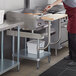 A woman using a Regency stainless steel equipment stand with a wooden cutting board in a commercial kitchen.