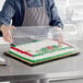 A person in an apron holding a Choice 1/2 Size Low Dome Sheet Cake Display Container with a cake inside.