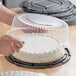 A person using a Choice 10" Low Dome Cake Display Container with a clear plastic lid to store a cake.