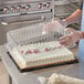 A person in a white apron placing a sheet cake in a Choice plastic container with a clear dome lid.