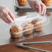 A person in gloves putting a muffin in a clear plastic container with a clear plastic lid.