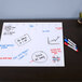 A Quartet white frameless glass dry erase desktop weekly planner with markers on it.