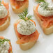 A group of small sandwiches with smoked salmon, cream cheese, and dill weed garnish.