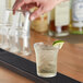 A person pouring a drink into a Duralex glass with ice and lime on a bar.